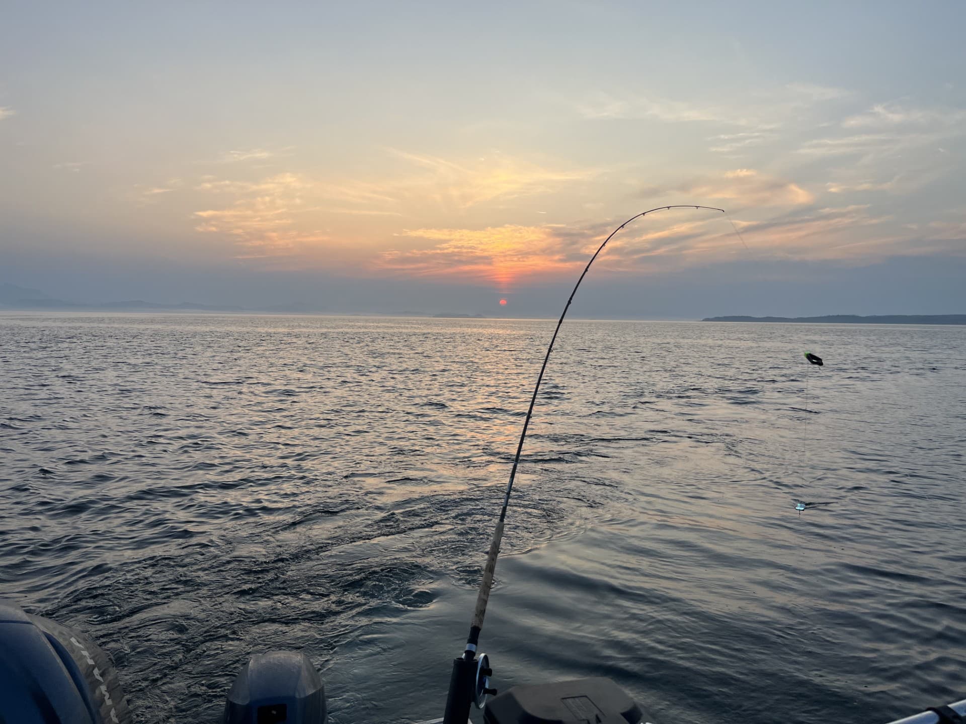 A fishing rod bent against a sunrise over the water