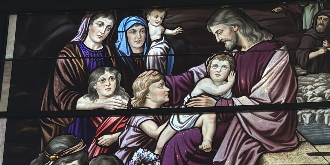 Stained glass window of Jesus welcoming and blessing the children